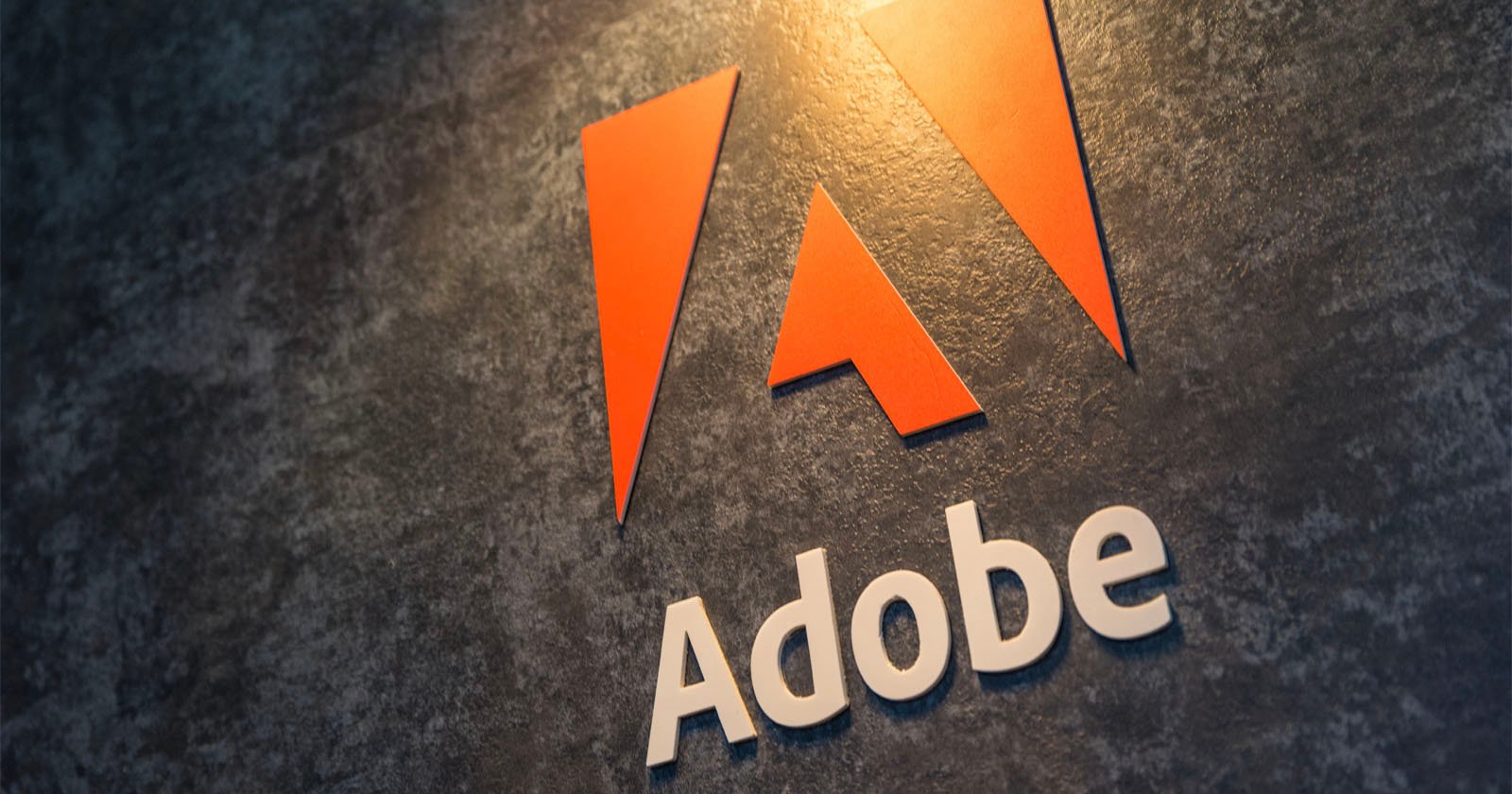 Close-up of the adobe logo with a stylized a in orange above the word adobe in white, affixed to a textured dark gray wall.