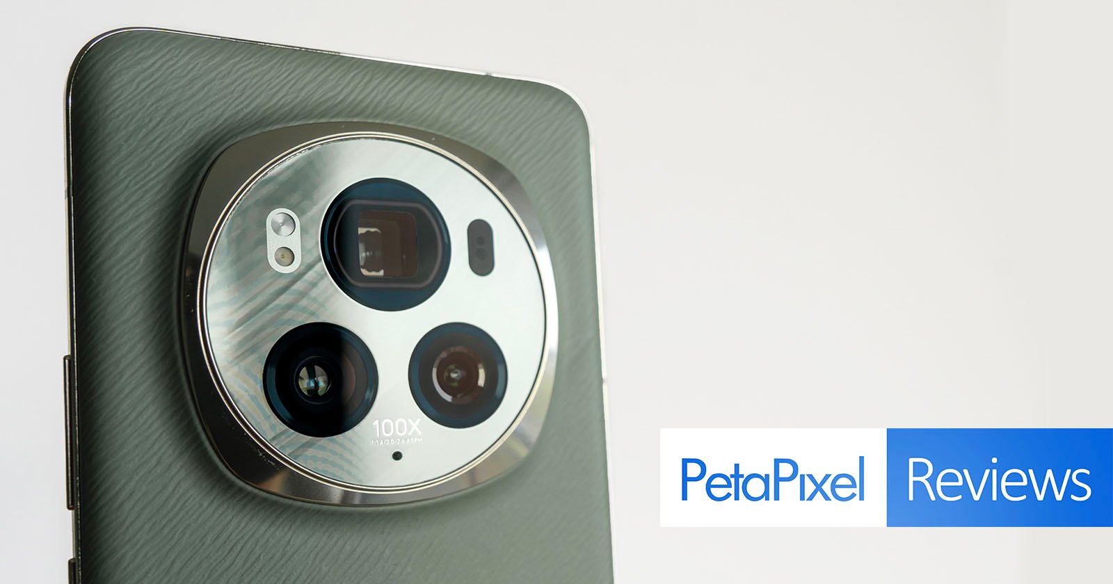 Close-up of a smartphone's camera setup featuring multiple lenses and 100x label, against a light grey background, with a petapixel reviews logo in the corner.